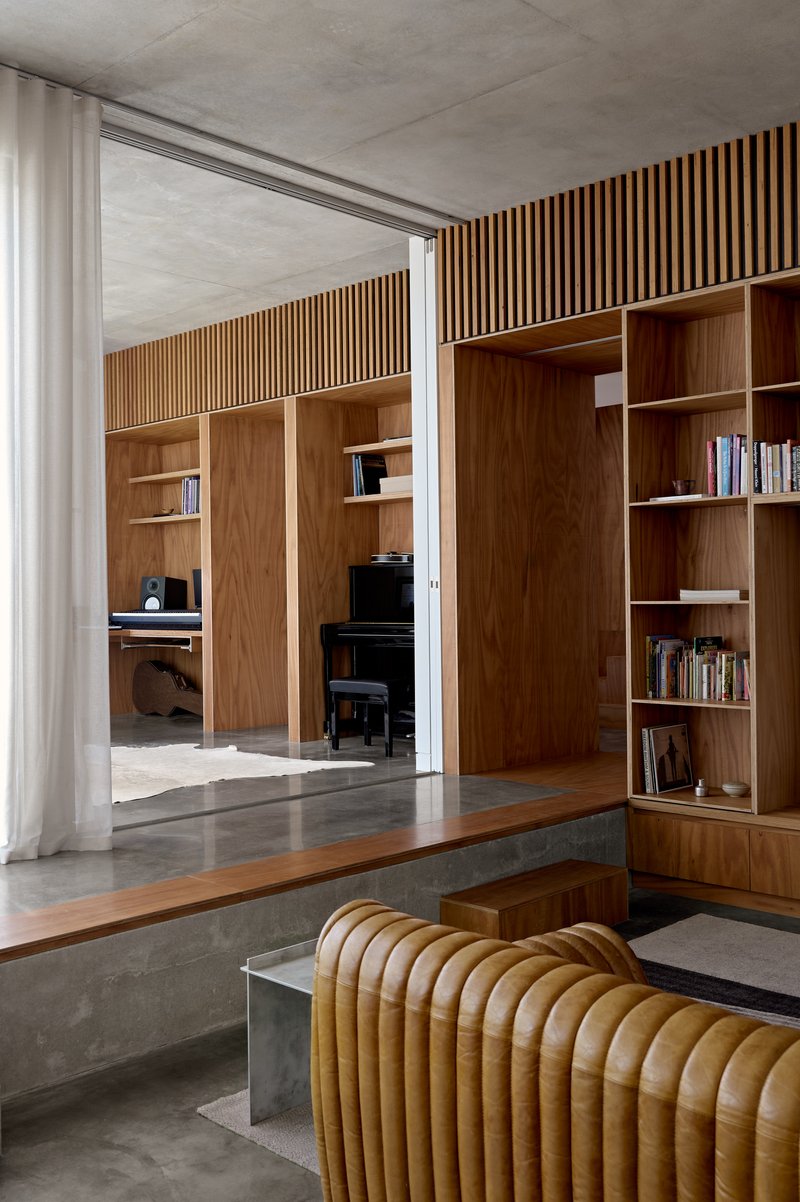Living area looking through to study with timber-slatted wall, built-in shelving, and polished concrete floor