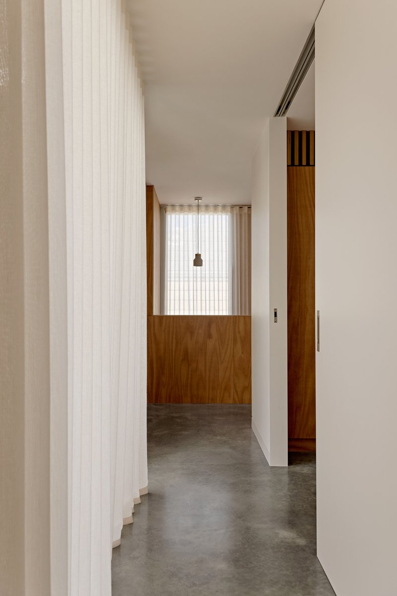 Hallway with polished concrete floor, white ribbed curtain and timber-clad partition under diffused daylight