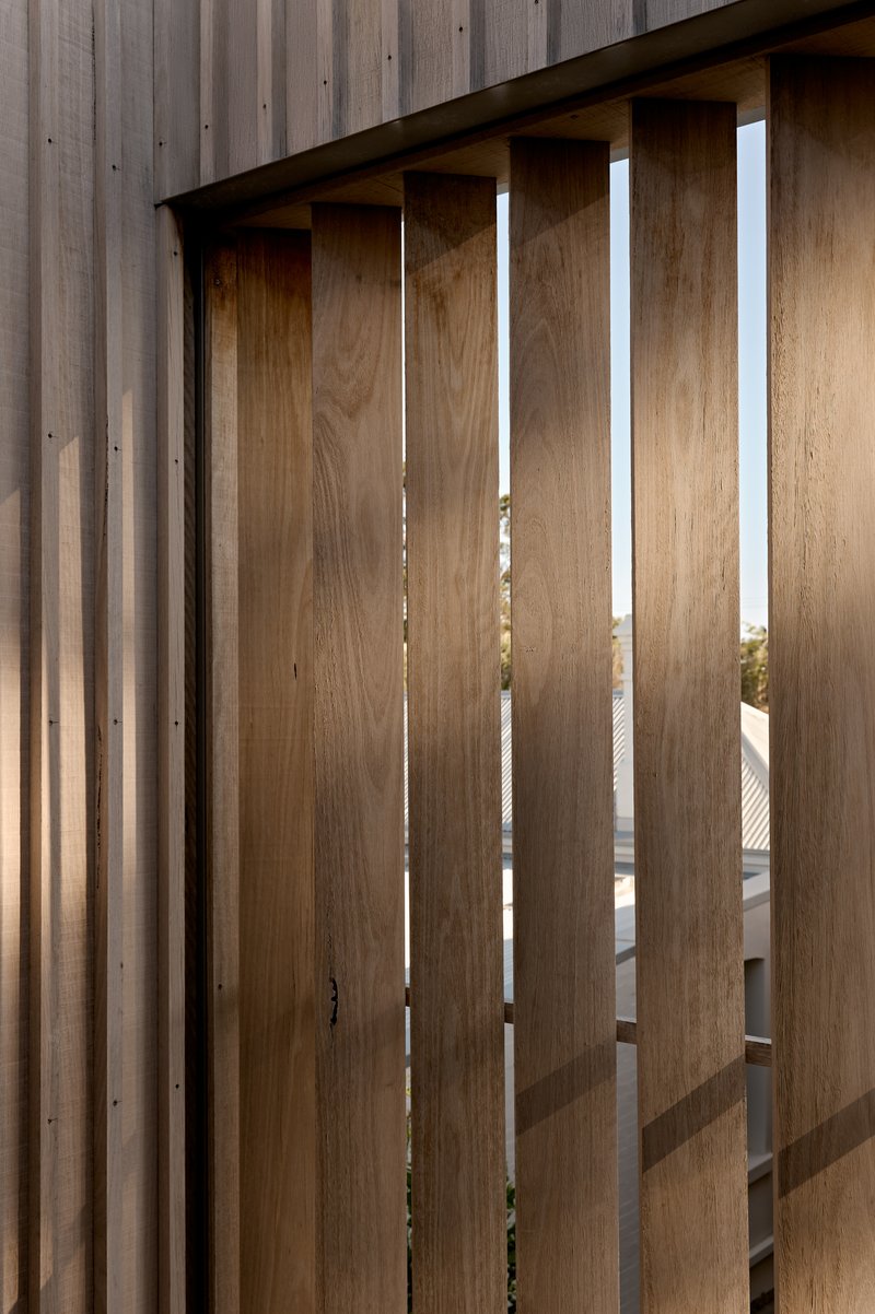 Vertical timber screen with evenly spaced slats filtering light onto a timber-clad wall