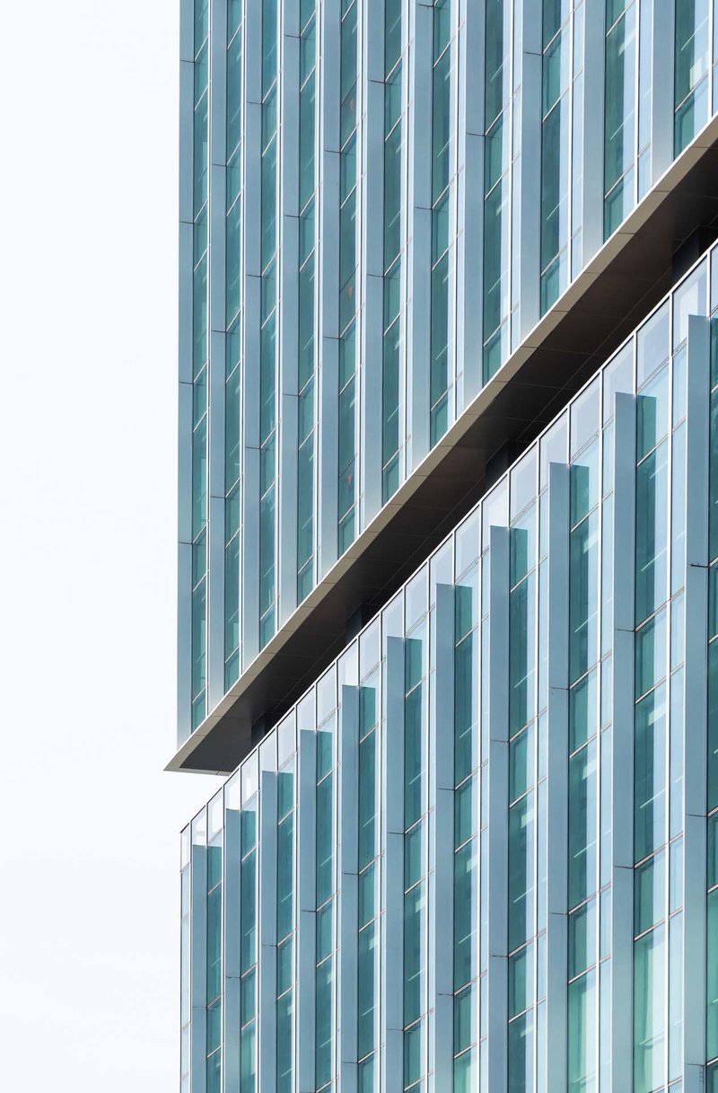 Close-up of vertical glass fins and diagonal canopy edge slicing across the tower facade