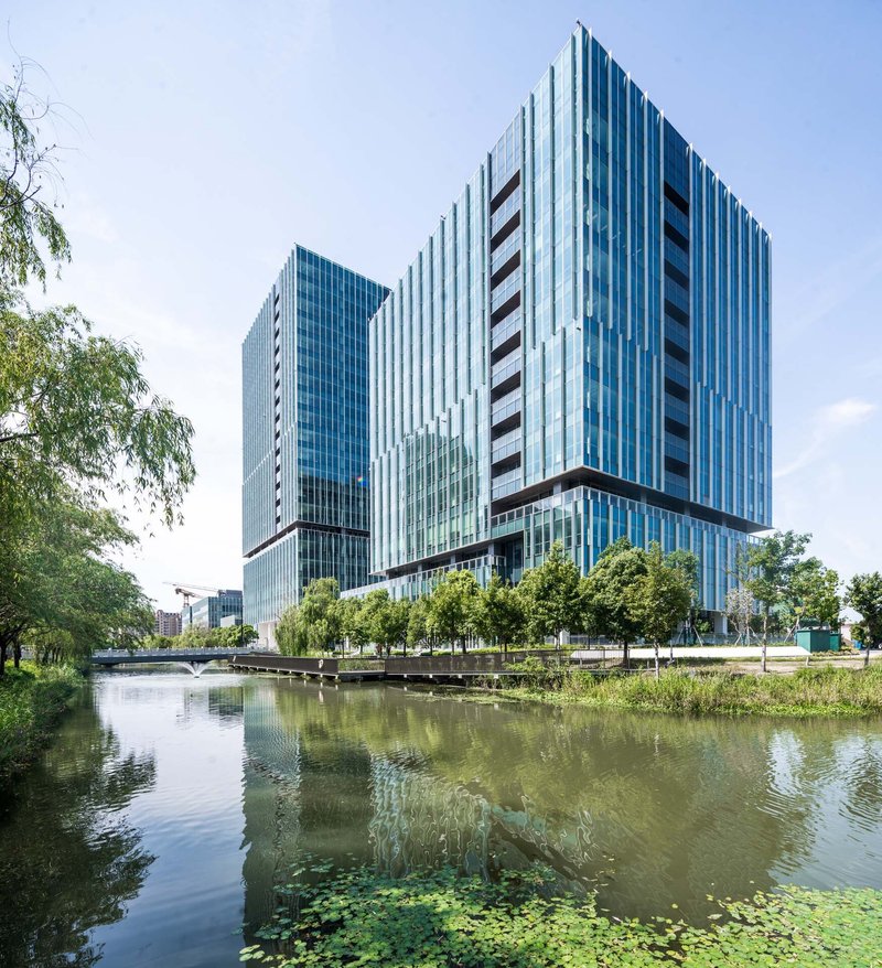 View across a pond with lily pads toward vertical glass and metal-clad towers