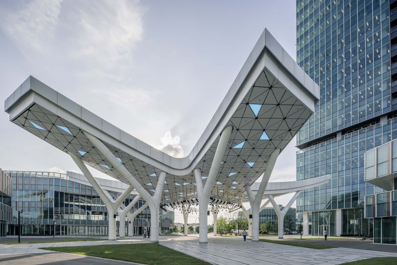 Elevated canopy with triangulated soffit and white branching columns spanning between glass towers