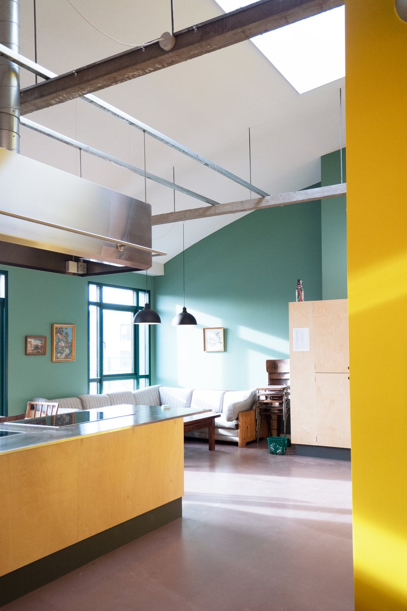 Open-plan living space with exposed timber beam, yellow column, and teal wall in bright daylight