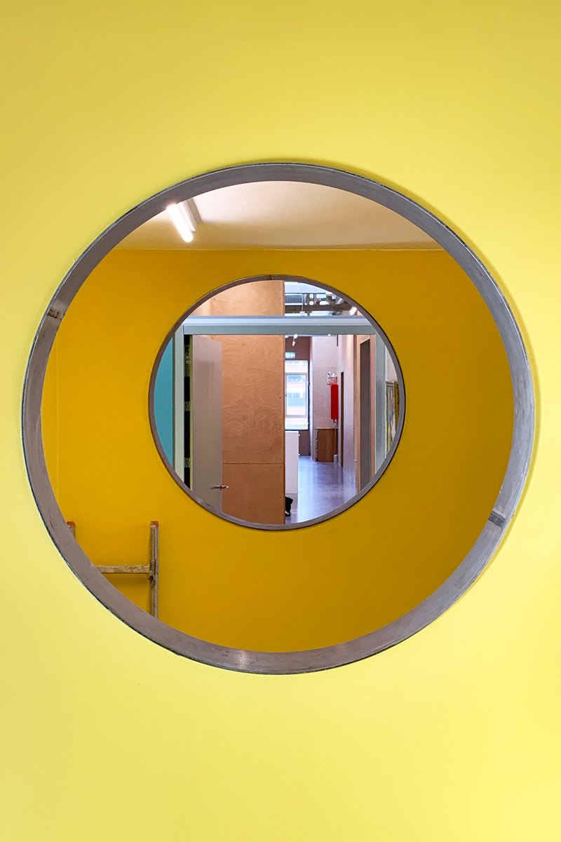 Circular yellow portal with metal frame offering a view through to plywood-lined corridor beyond