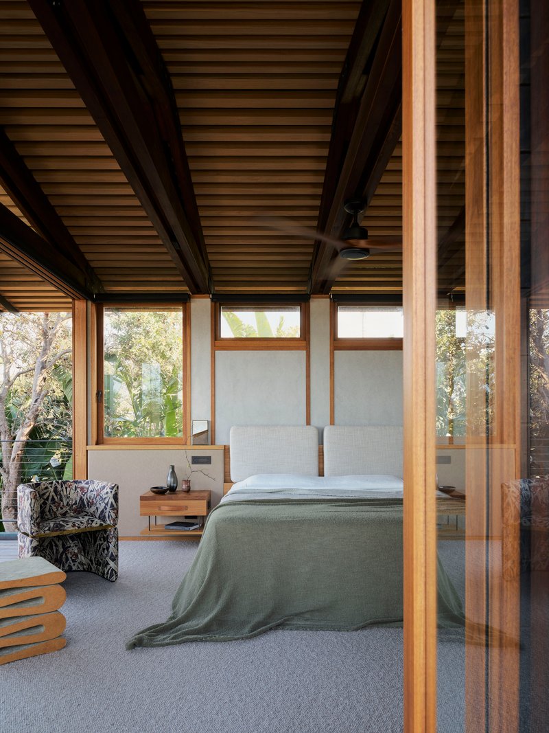 Bedroom with dark timber structure and continuous ribbon windows overlooking treetops