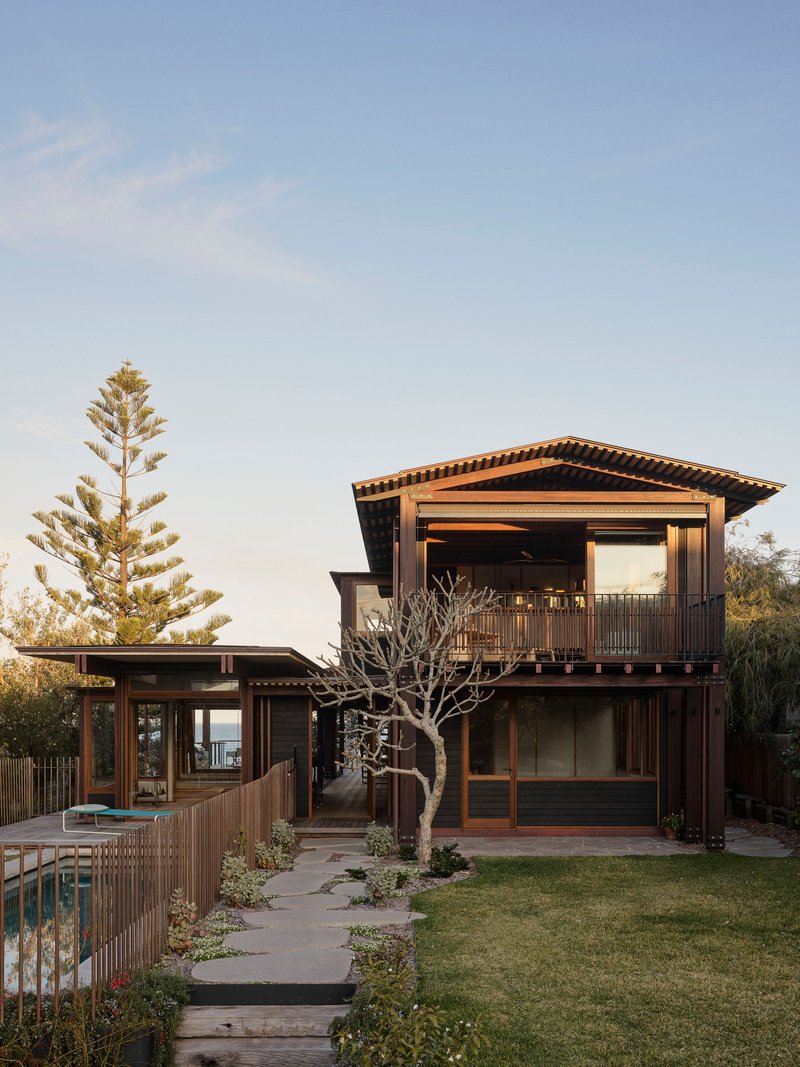 Garden view of timber-framed volumes with deep overhangs and a bare tree in the lawn