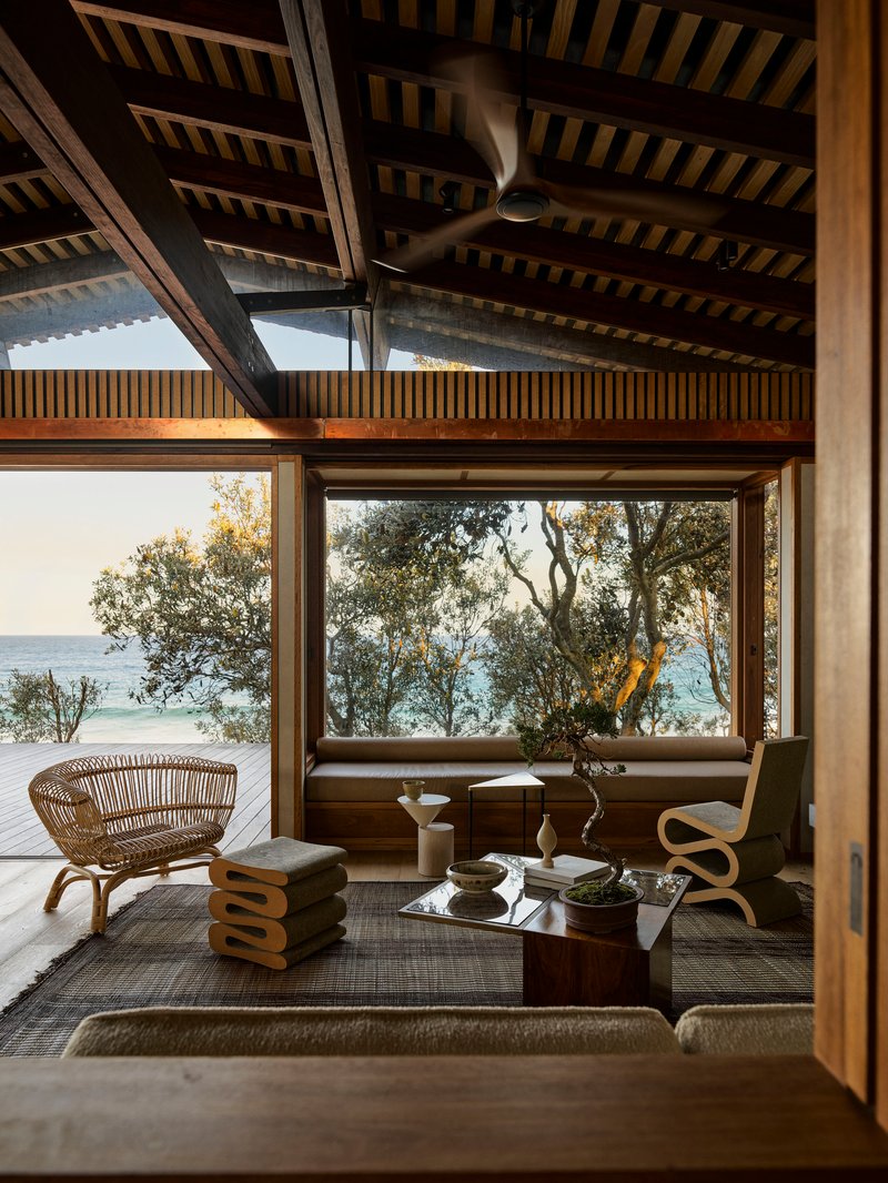 Glazed corner opening framing ocean views through coastal vegetation with slatted ceiling above