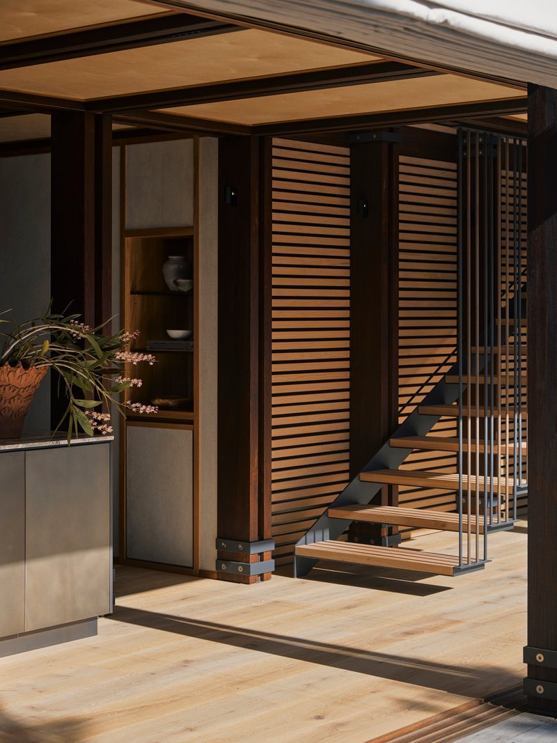 Open timber-framed threshold with horizontal slatted screens flanking a steel and wood staircase