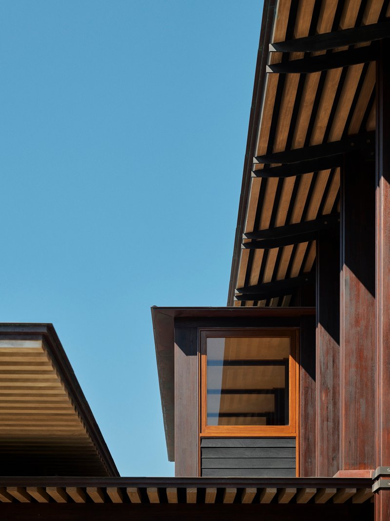 Exterior view of stacked timber volumes with slatted cladding and cantilevered roof overhang against clear sky