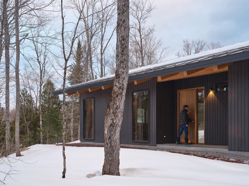 Exterior passageway with vertical siding, exposed timber brackets, and figure walking through at dusk