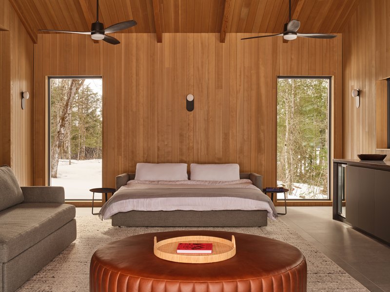 Bedroom interior with vertical wood paneling and two glazed doors framing winter forest views