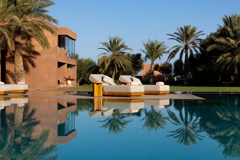 Pool reflecting palm trees and the terracotta volumes with white loungers on the timber deck