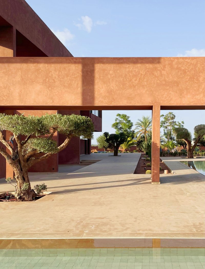 Ochre-coloured horizontal beam framing a courtyard with olive trees and stone paving