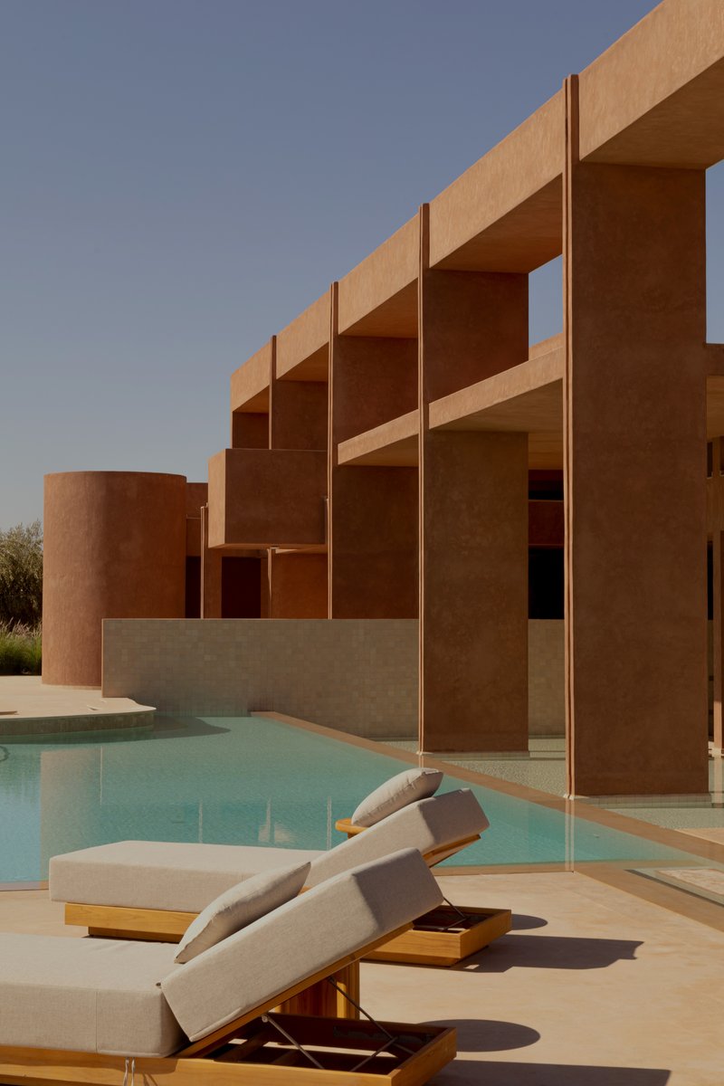Poolside terrace with lounge chairs beneath the rammed earth pergola structure at dusk