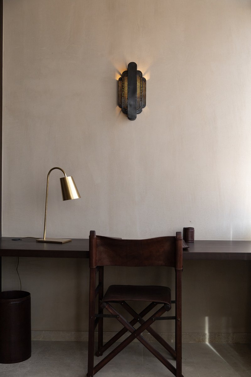 Interior workspace with timber chair, brass desk lamp and perforated metal wall sconce