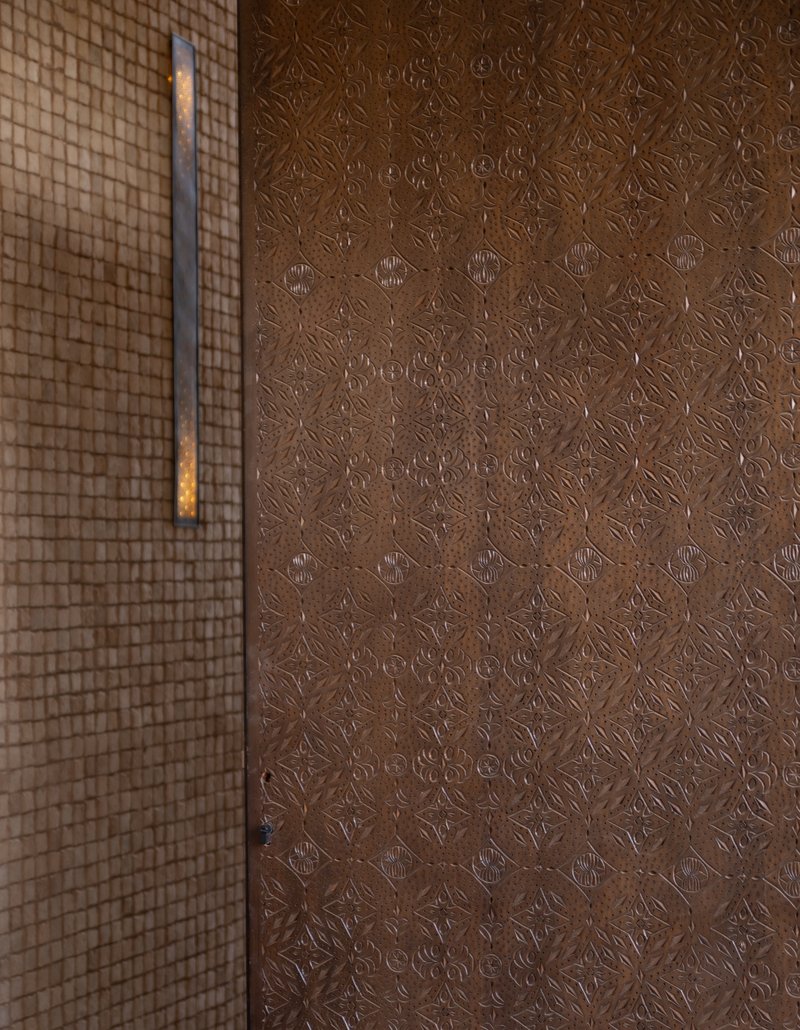 Embossed metal door panel with geometric pattern beside a gridded screen wall in low light