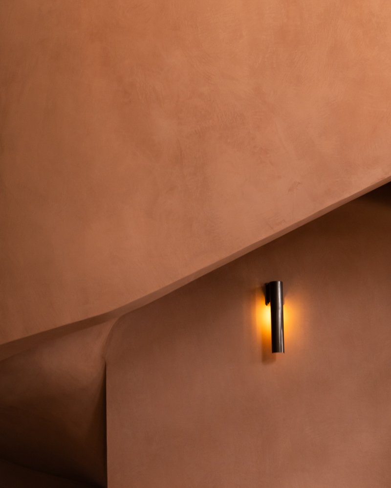Cylindrical wall sconce casting golden light on a curved plaster wall above a rounded opening