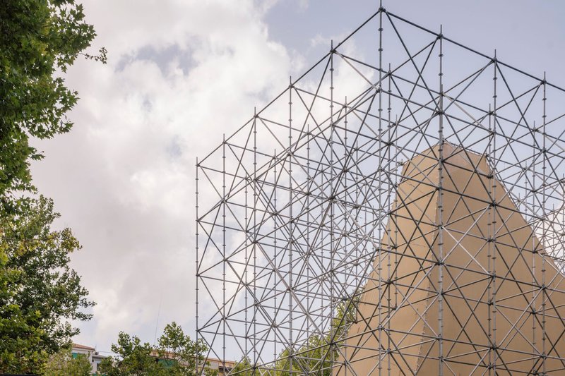 Detail of the steel truss framework rising against a cloudy sky with tree branches visible