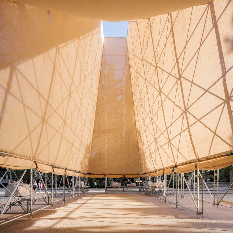 View under the tented roof with sunlight filtering through the fabric and scaffold framework below