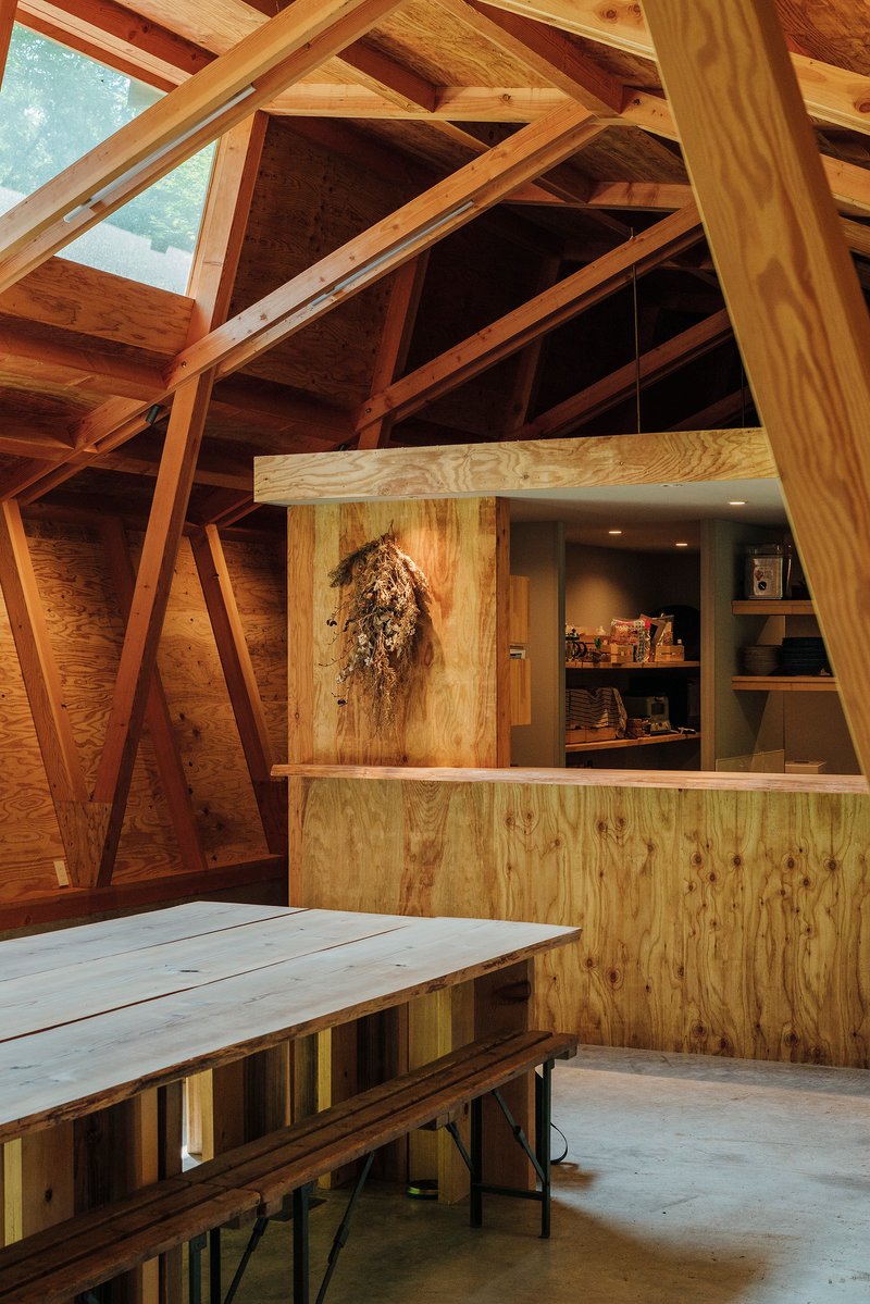 Plywood service counter beneath diagonal timber columns and exposed roof framing with dried flowers hanging on wall