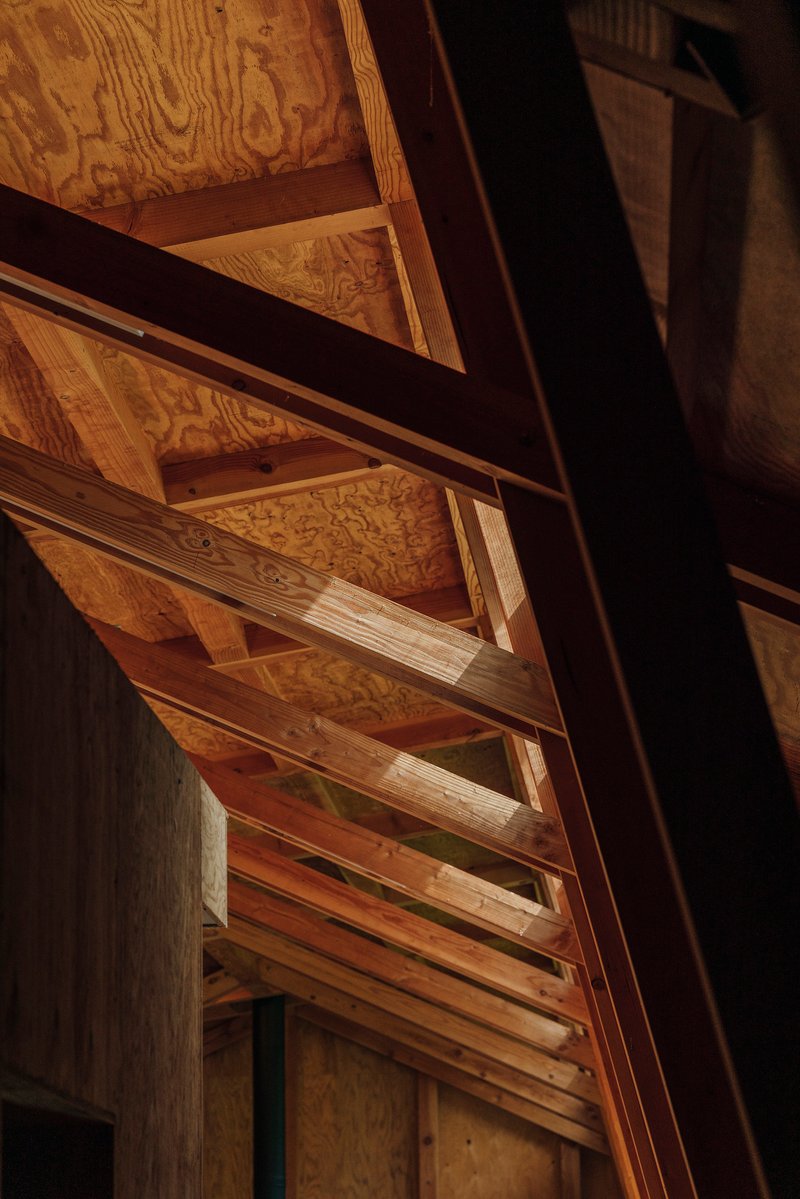 Detail of exposed wooden beams and plywood panels meeting at angled structural joints in warm light