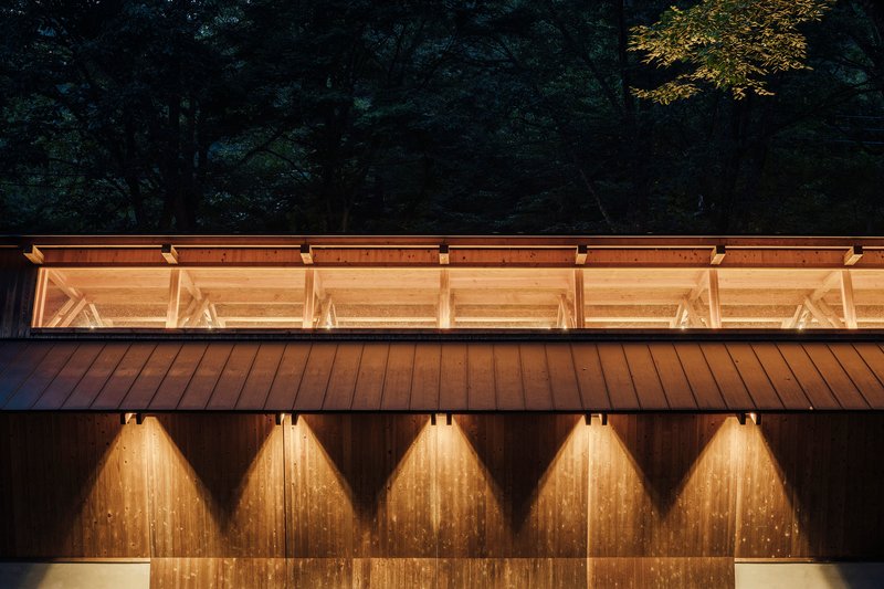 Night view of clerestory windows and illuminated diagonal timber braces above weathered metal cladding