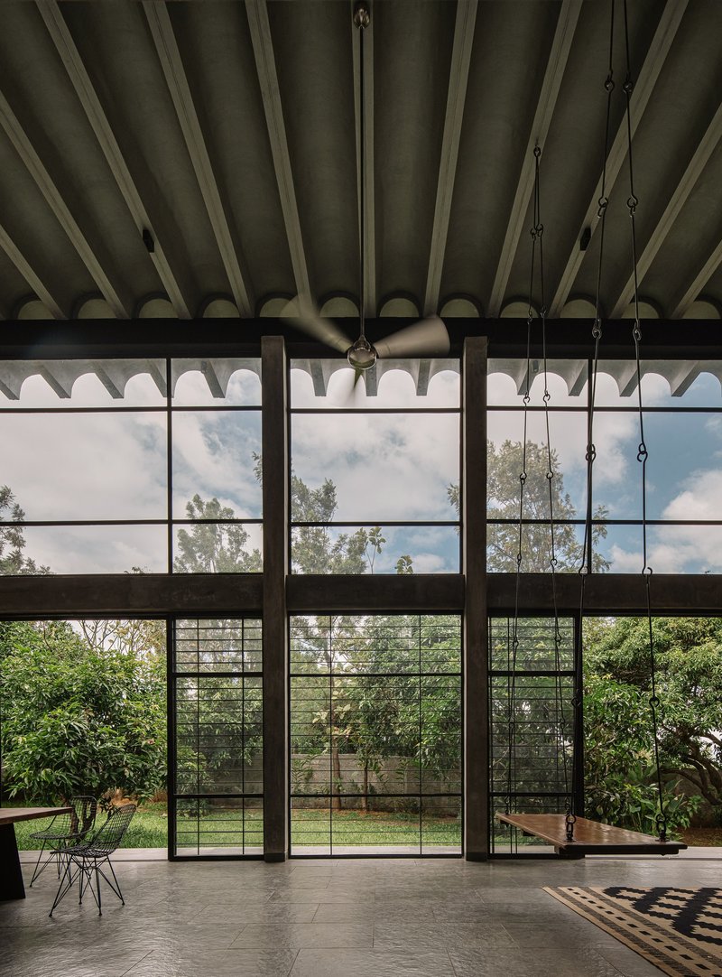 Double-height interior with steel-framed glazing beneath exposed diagonal timber roof trusses and suspended ceiling fan