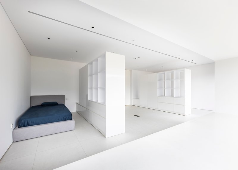 Open-plan bedroom alcove with bed and freestanding white partition wall dividing space from adjacent storage area