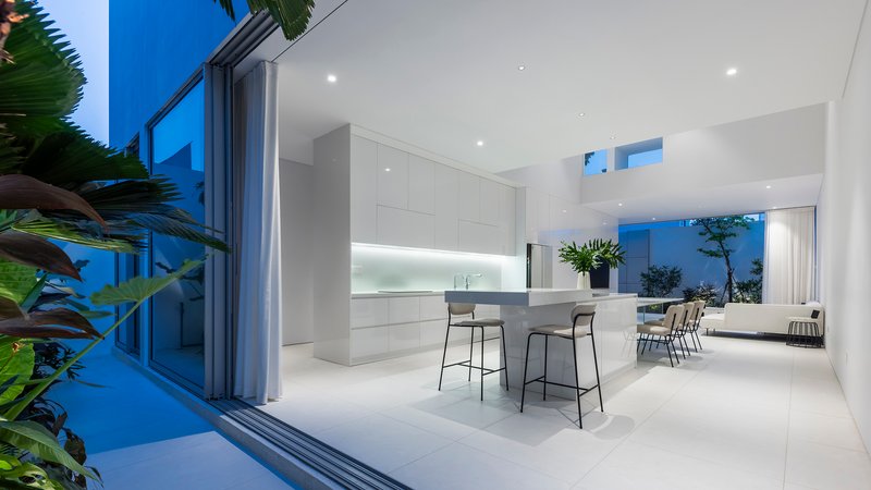 Open kitchen and dining area at dusk with bar stools and sliding glass doors framing tropical plants