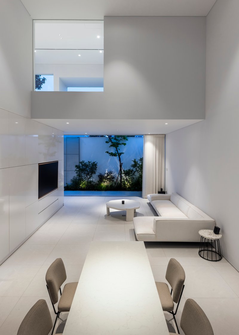 Double-height living room at dusk with suspended mezzanine and garden courtyard view through floor-to-ceiling glazing