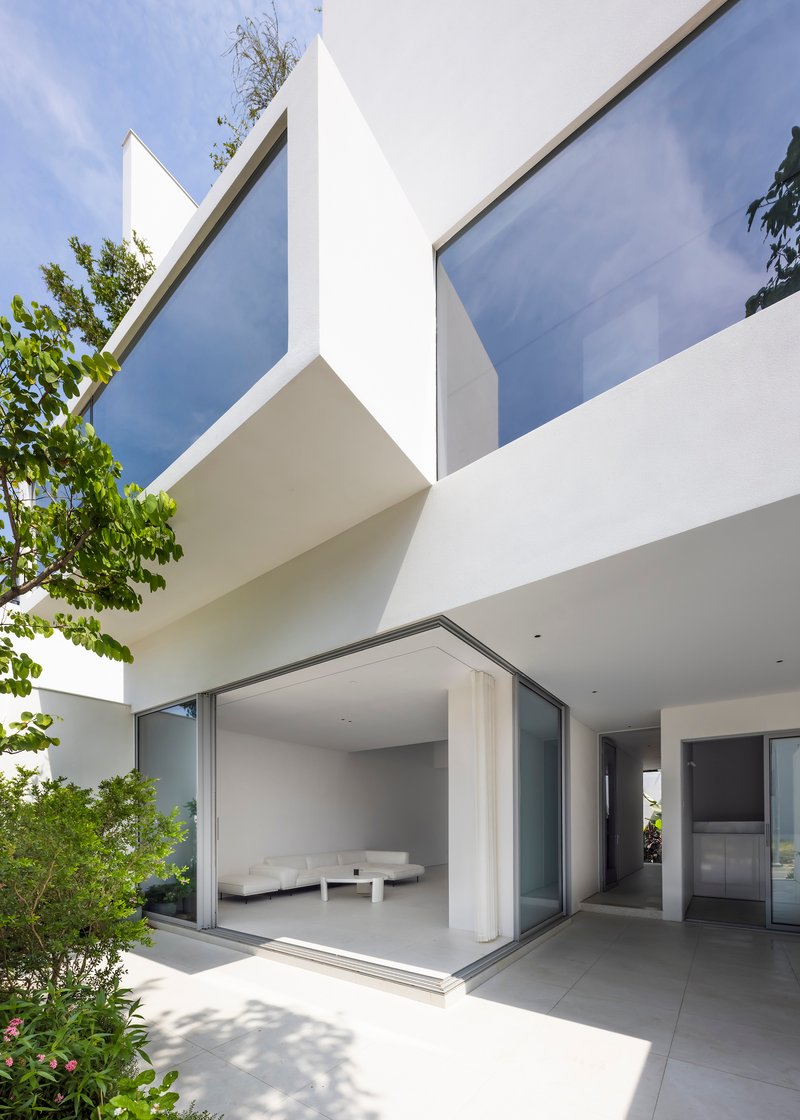 Ground floor terrace with sliding glass doors opening to the interior and trees framing the white volumes above