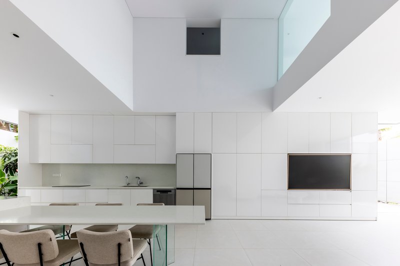 Double height void above the white kitchen and dining table with view to upper skylight