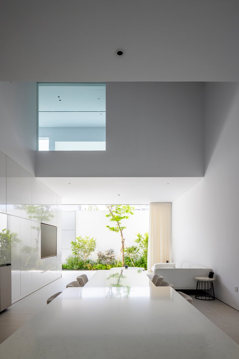 Dining area with mezzanine void overhead and planted courtyard visible through the glass wall