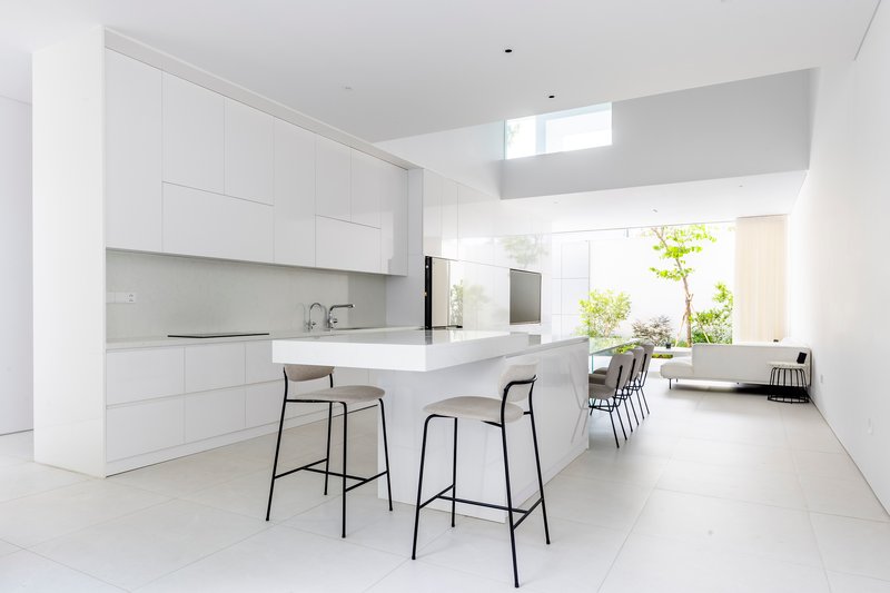 Kitchen with white cabinetry and island beneath clerestory window with view to planted courtyard