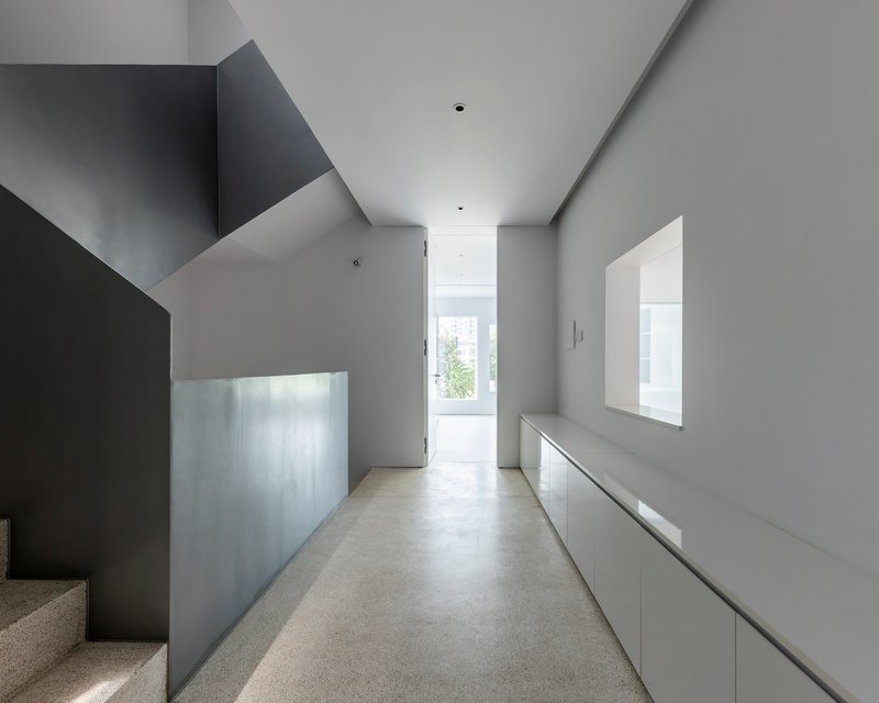 Upper level corridor with angled ceiling planes and terrazzo flooring leading to window