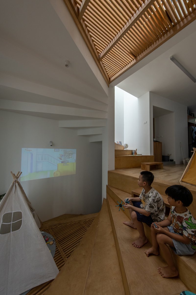 Double-height space with slatted timber ceiling and two children seated on the stepped platform