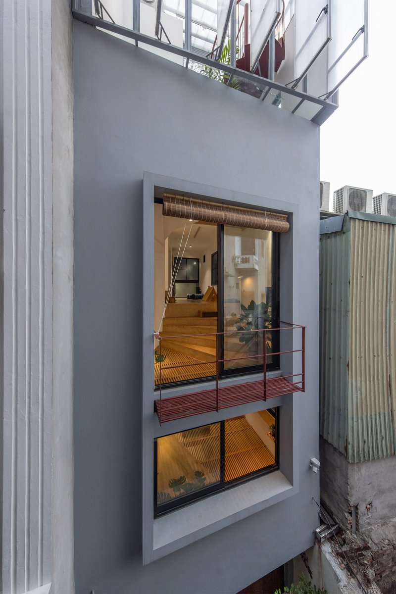 Exterior facade showing stacked glazed openings and a red metal balcony between neighbouring walls at dusk