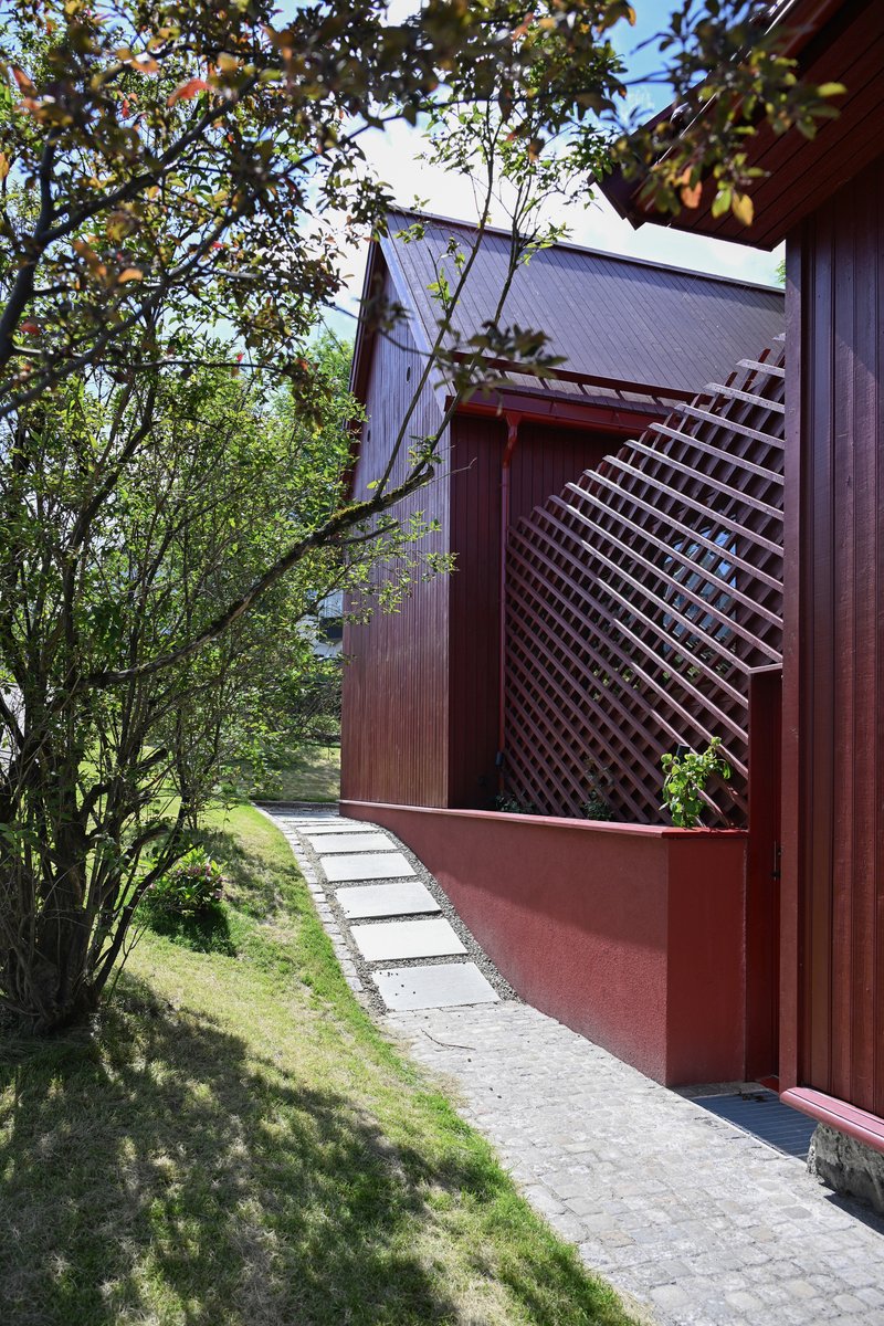 Red timber slatted screen and cladding along a stone paved pathway beneath leafy tree branches
