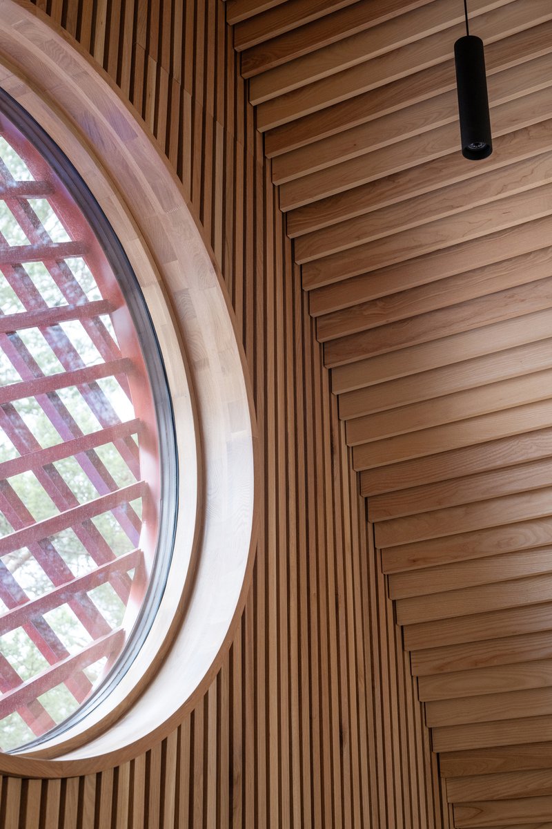 Circular window with gridded timber screen framed by vertical wood slats and horizontal ceiling battens