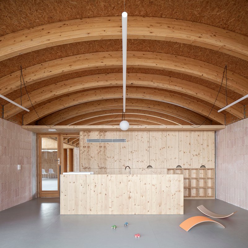 Interior space with curved laminated timber arches and a plywood island beneath suspended pendant lighting