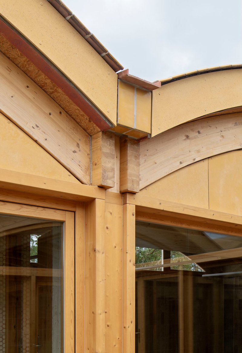Detail of timber post and beam junction with yellow hempcrete panels and exposed laminated timber arches
