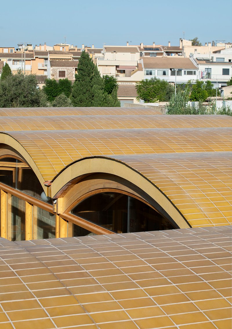 Undulating tiled roof in ochre yellow ceramic with residential buildings visible in the background