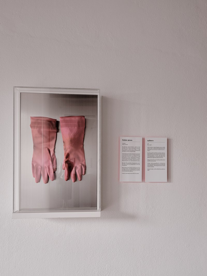 White display box containing pink rubber gloves mounted on a wall with text panels