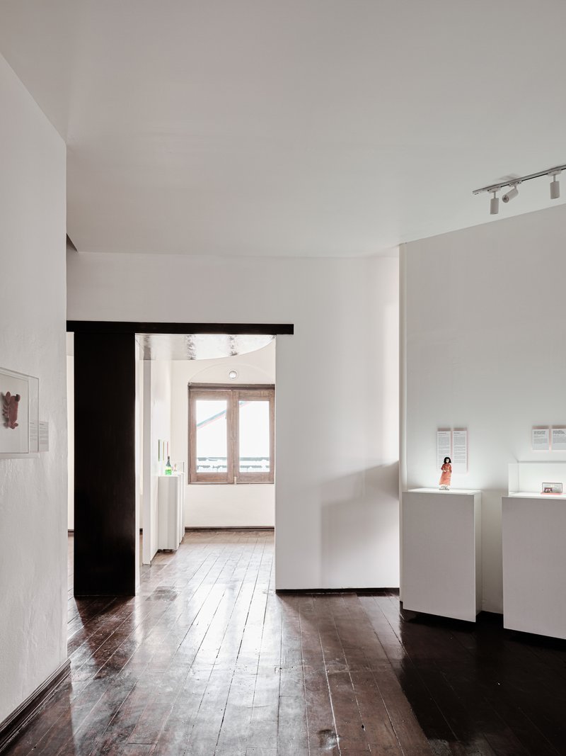 Gallery corridor with a black timber doorframe opening to a sunlit room with timber window shutters