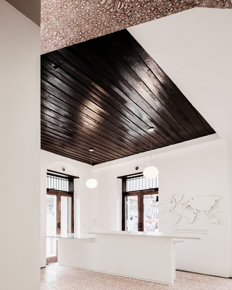 Reception desk under a dark timber slatted ceiling with patterned tile above and sphere pendant lights