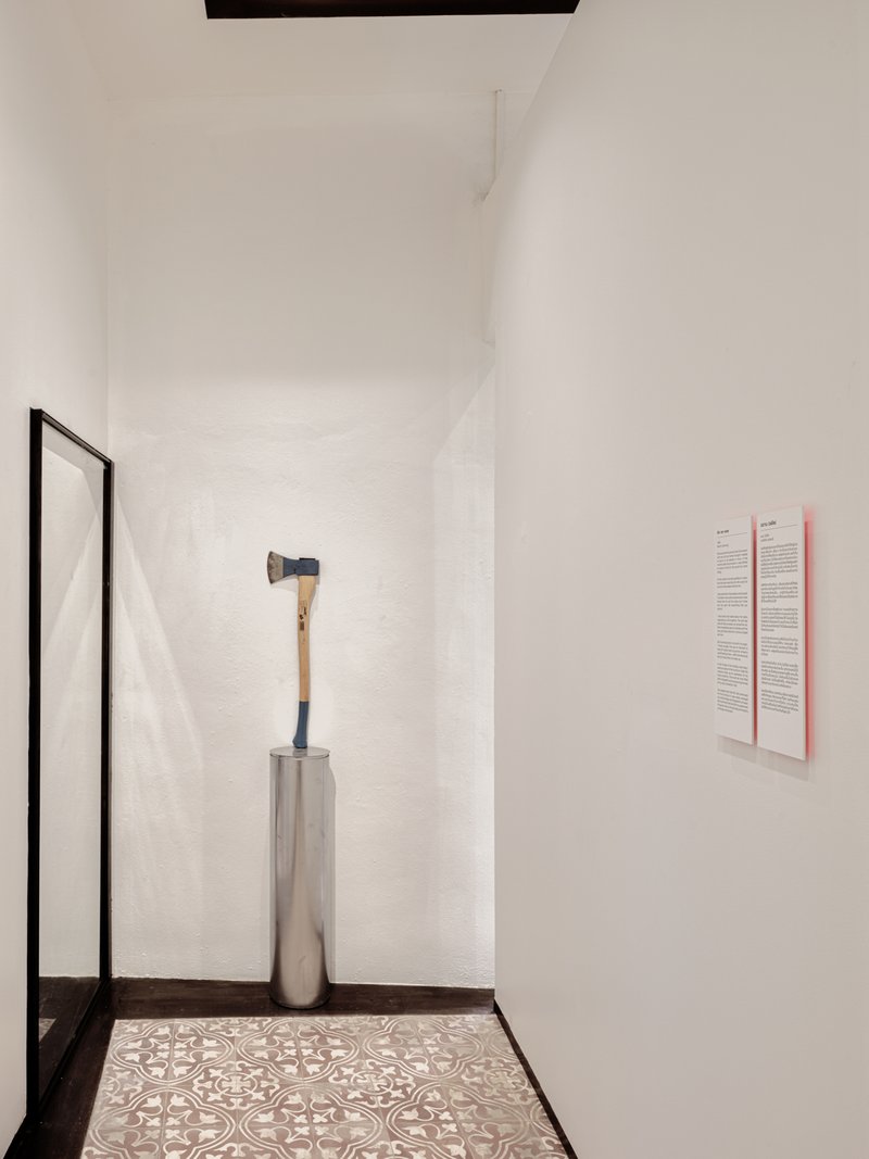 Corner alcove with patterned floor tiles and a hammer displayed on a cylindrical pedestal