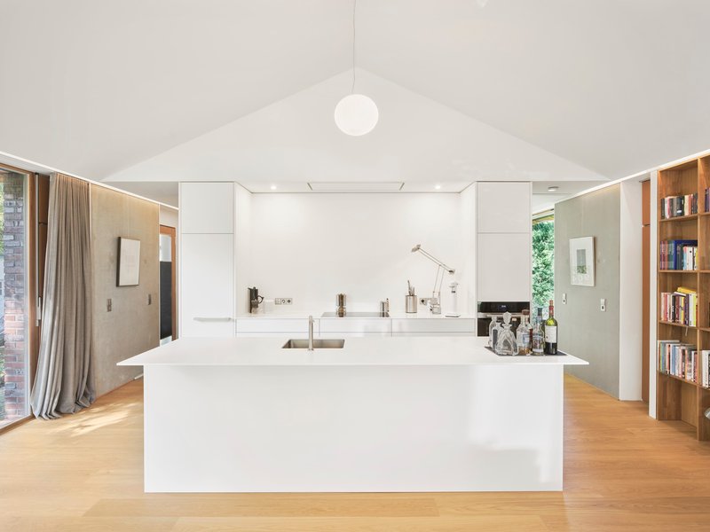 White kitchen island beneath vaulted ceiling with spherical pendant light and continuous perimeter slot lighting