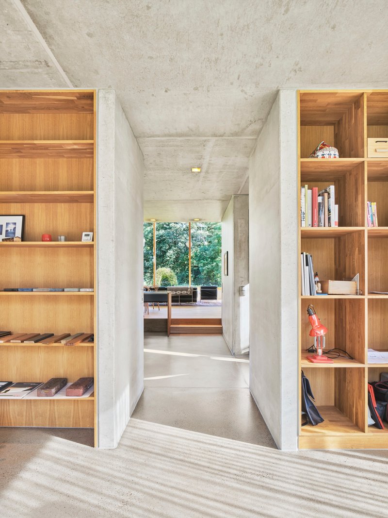 Interior hallway with exposed concrete ceiling flanked by built-in timber bookshelves and garden view beyond