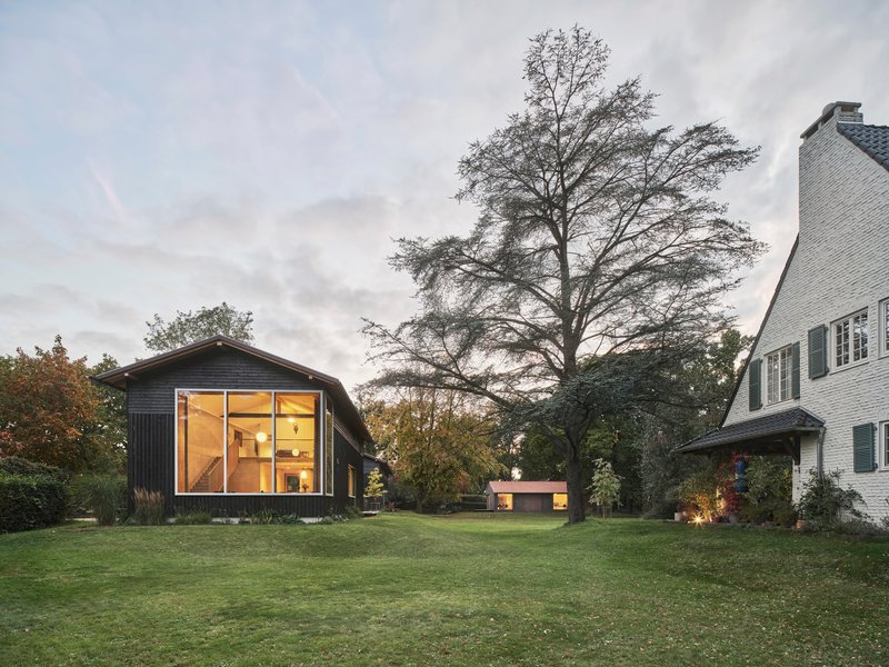 Garden elevation showing two gabled volumes beneath a large deciduous tree at dusk