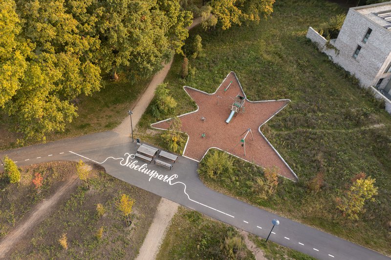 Overhead view of a star-shaped red rubber playground surface bordered with white edging and play equipment